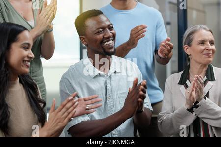 Un giovane uomo d'affari che applaude con i suoi colleghi in ufficio. Foto Stock