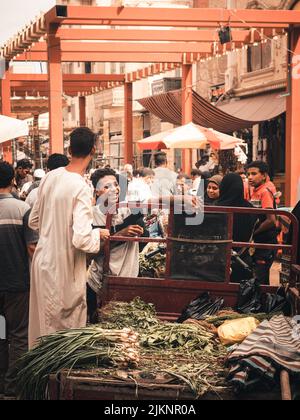 Un colpo verticale di un venditore di strada che indossa galabeya che vende verdura in un mercato locale del traffico ad Assuan, Egitto Foto Stock