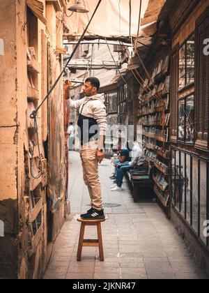 Una bella foto di un artista medio orientale adulto che si erge su una piccola sedia di legno e dipinge in una vecchia strada stretta ad Assuan, Egitto Foto Stock