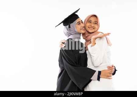 Felice studentessa asiatica laureata indossando toga abbracciando la sua amica Foto Stock