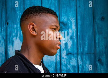 Una vista laterale di un uomo nero in abiti casual su una parete blu sfondo guardando avanti Foto Stock