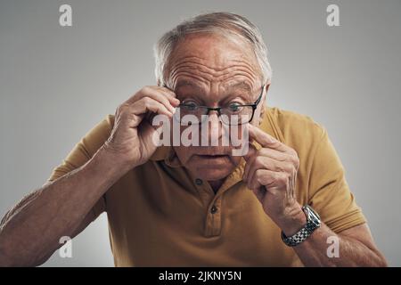 Im sicuramente diventare vecchio. Studio girato di un uomo anziano che regola i suoi occhiali su uno sfondo grigio. Foto Stock