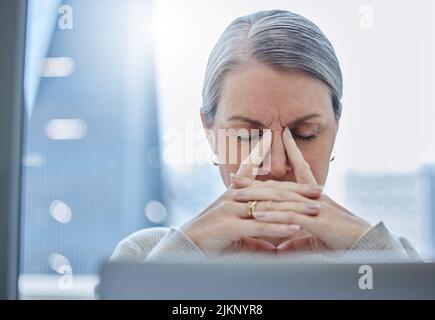 Questo non mi va a modo mio: Una donna d'affari matura seduta da sola in ufficio e sentendosi stressata. Foto Stock