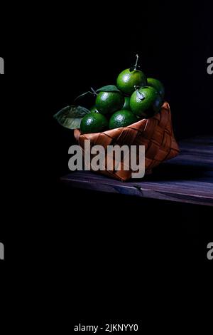 Un colpo verticale di mazzo di lime verdi in cesto su legno isolato su sfondo nero Foto Stock