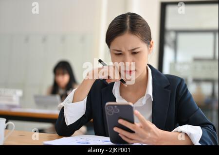 Ha sottolineato la giovane donna d'affari asiatica o la donna di ufficio che ha un problema sul suo smartphone, ricevendo una e-mail scioccata. Foto Stock