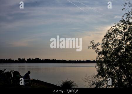 Persone sedute su sedie a sdraio da un lago al tramonto Foto Stock