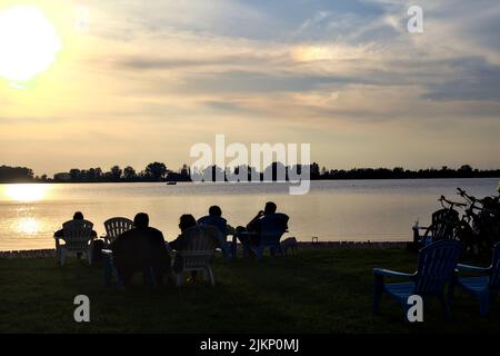 Persone sedute su sedie a sdraio da un lago al tramonto Foto Stock