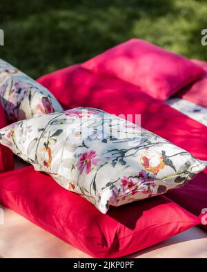 Un luminoso colpo verticale di lenzuola e cuscini floreali e rosa sull'erba per un picnic Foto Stock