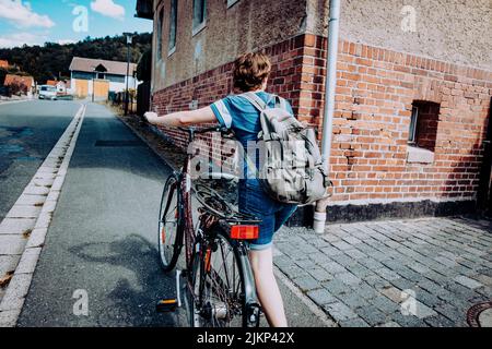 Un ciclista che porta la sua bicicletta attraverso uno stretto sentiero circondato da vecchi edifici in mattoni Foto Stock