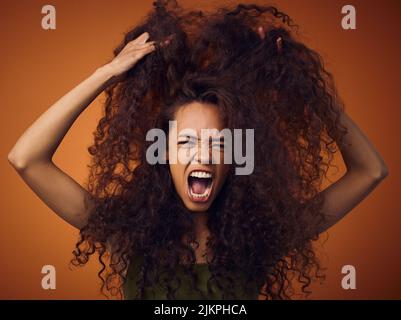Non mi importa, im appena avere un giorno difettoso dei capelli. Una donna con capelli ricci ritenere frustrati mentre si levano in piedi su uno sfondo arancione. Foto Stock