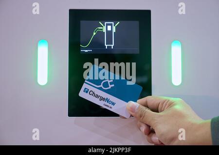 Primo piano di un uomo d'affari che utilizza la smart card touch sul sensore monitor per batteria ricaricabile ai veicoli elettrici o auto EV Foto Stock
