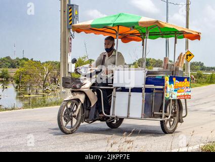 SAMUT PRAKAN, THAILANDIA, 01 2022 GIUGNO, un distributore di gelati percorre una moto a tre ruote lungo una strada del villaggio Foto Stock