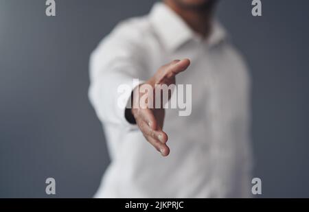 Agita su di esso. Un uomo d'affari irriconoscibile che si alza da solo su uno sfondo grigio ed allunga la mano per una stretta di mano. Foto Stock