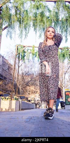 Una foto verticale di una bella giovane donna che indossa un abito floreale in posa all'aperto Foto Stock