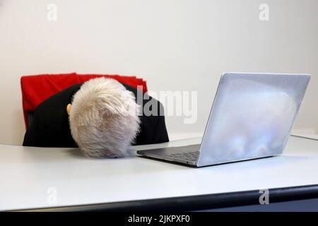 Donna con capelli corti tinti che dorme vicino al portatile al tavolo dell'ufficio. Concetto di lavoratore sovraccaricato, stanco dopo il lavoro, pigro giorno Foto Stock