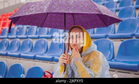 Signora pensiva con ombrello che tocca il mento e guarda via sulla tribuna Foto Stock