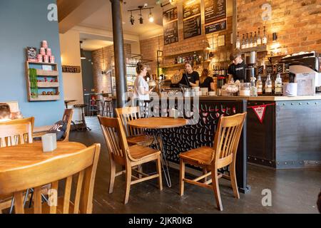 Personale giovane femminile e maschile, che lavora all'interno di una caffetteria Lancashire a Ramslbottom, Lancashire, Inghilterra, che serve caffè e camerate Foto Stock