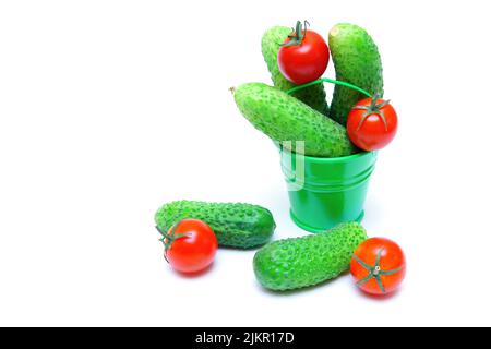 Piccolo secchio verde con cetrioli appena raccolti e pomodori ciliegini isolati su sfondo bianco. Foto Stock