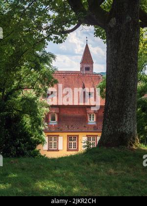 Una bella vecchia guglia chiesa è incorniciata dal fogliame estivo alla periferia di Wissembourg, una bella città nella regione del basso Reno in Francia. Foto Stock