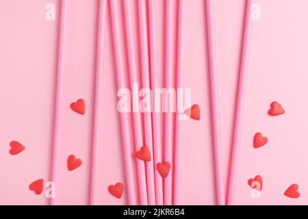 Sfondo di San Valentino fatto di paillette di carta da bere rosa e cuori dolci commestibili su sfondo rosa. Foto Stock