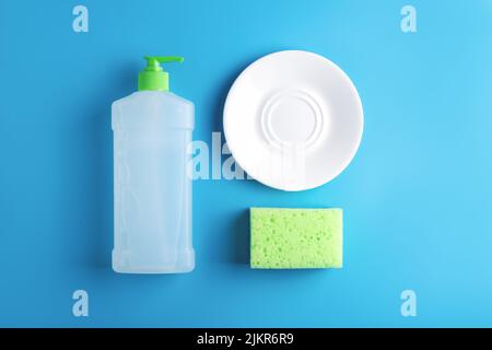Composizione della cucina con lastra bianca di vetro pulita, spugna per la pulizia verde e bottiglia di sapone per piatti disposti su sfondo blu. A disposizione piatta, nuclei familiari. Foto Stock
