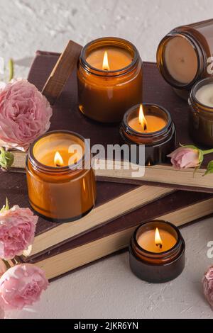 Un set di candele aromatiche diverse in vasetti di vetro marrone. Candela profumata fatta a mano. Le candele di soia stanno bruciando in un vaso. Aromaterapia e relax in spa e casa. Fuoco in vaso marrone. Foto Stock