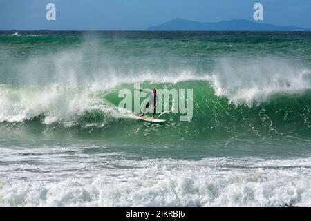 Un surfista corre un'onda al Monte Maunganui, Nuova Zelanda, una delle spiagge da surf più popolari del paese. Sullo sfondo è Mayor Island Foto Stock