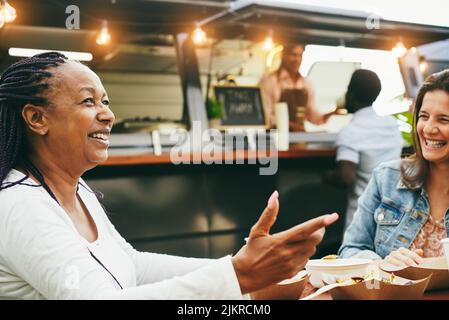 Felice multirazziale donne anziane che mangiano al ristorante di camion di cibo all'aperto - fuoco sul volto femminile africano Foto Stock