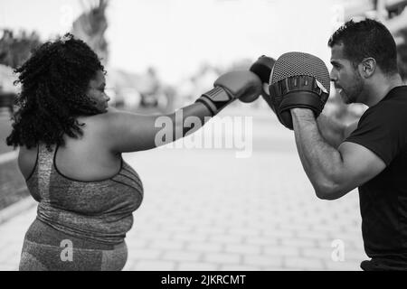 Donna curvy africana e personal trainer fare boxing sessione di allenamento outdoor - Focus on man guanto - editing in bianco e nero Foto Stock