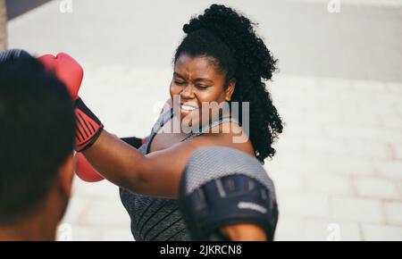 Donna curvy africana e personal trainer fare boxing sessione di allenamento all'aperto - concentrarsi sul viso Foto Stock