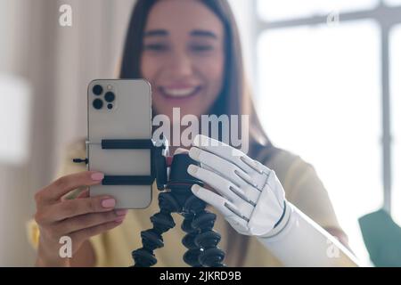 Blogger ragazza con braccio bionico utilizzando il telefono, live streaming di social media a casa, donna con disabilità conduce la vita attiva normale protesi artificiale Foto Stock