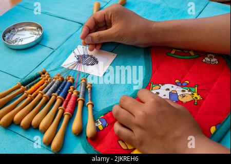 Mani di bambino che fanno merletto della bobina. Fili colorati di pizzo. Abilità e creatività. Foto Stock