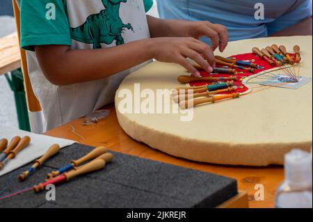 Mani di bambino che fanno merletto della bobina. Fili colorati di pizzo. Abilità e creatività. Foto Stock