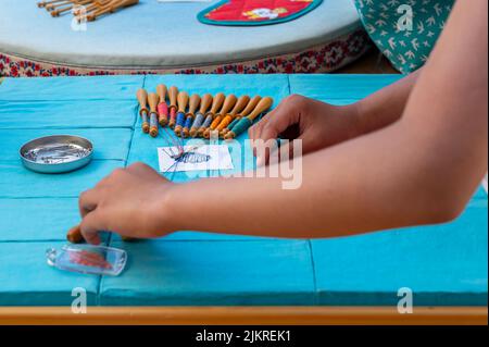 Mani di bambino che fanno merletto della bobina. Fili colorati di pizzo. Abilità e creatività. Foto Stock