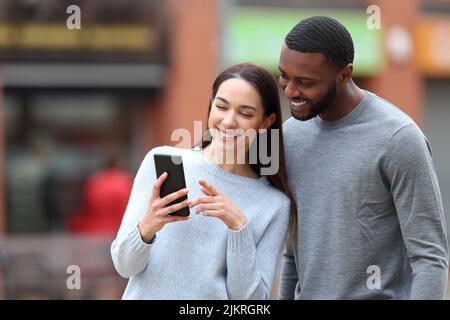 Felice coppia interrazziale controllare il telefono cellulare in strada Foto Stock