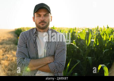 Coltivatore bearded in un cappello e una camicia a quadri sullo sfondo di un campo di mais Foto Stock