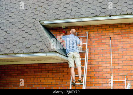 Uomo proprietario di casa di lavoro di ridipingere casa con pennello e vernice bianca all'aperto in estate. Foto Stock