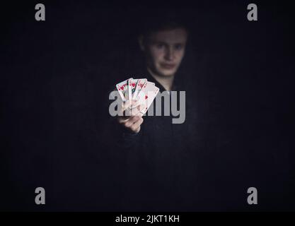 Il giocatore di poker di successo tiene in su una combinazione di colore reale vincente. Fortunato giocatore con carte da gioco su sfondo scuro. Vincitore del torneo di casinò, v Foto Stock