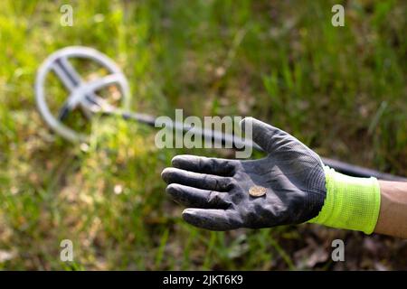 sul palmo di un guanto si trova una moneta con un metal detector wireless. sullo sfondo, la bobina del metal detector si trova al centro del telaio. a. Foto Stock