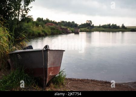 Una barca a motore è parcheggiata sulla riva di un lago o di un fiume in serata al tramonto o al mattino presto. La barca si trova in un luogo tranquillo vicino alla canna Foto Stock