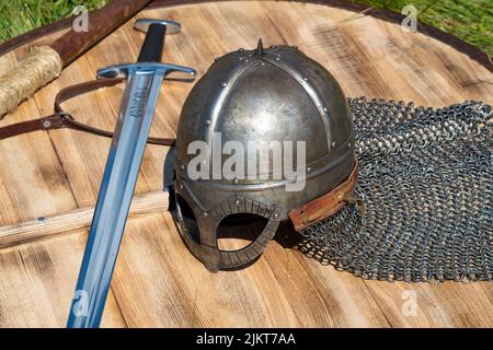 Casco di tipo normanno (casco vichingo) e spada scandinava giacciono su uno scudo di legno. Festa storica Foto Stock