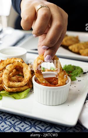 Un colpo verticale di una donna che mangia gustosi anelli di cipolla croccanti con salsa Foto Stock