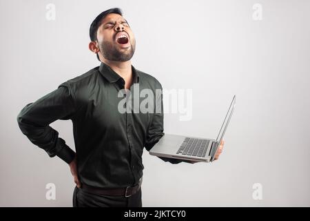 giovane indiano indossare uomo formale che soffre di dolore al midollo spinale dopo aver lavorato sul laptop Foto Stock