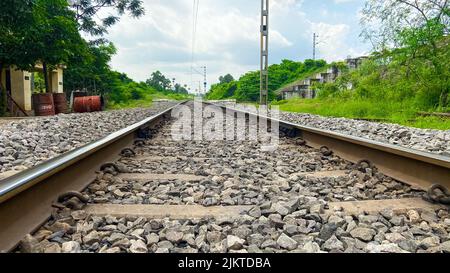 Un primo piano di ciottoli sulla ferrovia circondata dal verde in una giornata nuvolosa Foto Stock