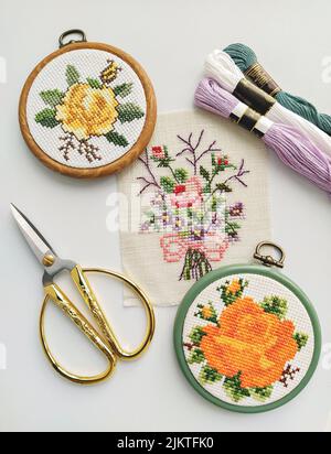 Cerchi, forbici, ago, filo e tessuto vintage in legno da ricamo con cuciture a croce floreali su disegno bianco e piatto Foto Stock