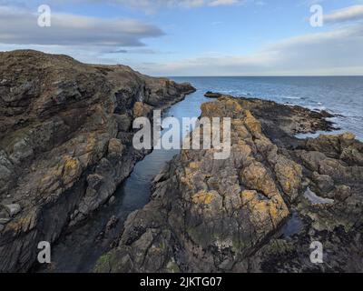 Un piccolo ruscello d'acqua proveniente da un mare che scorre attraverso la costa rocciosa Foto Stock