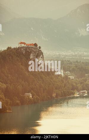 Uno scatto verticale di alcune case poste su una scogliera circondata da alberi sullo sfondo delle montagne. Foto Stock