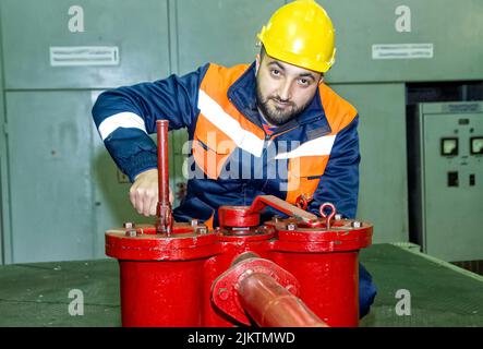 Un uomo caucasico che lavora su un'attrezzatura nella sua divisa e casco Foto Stock