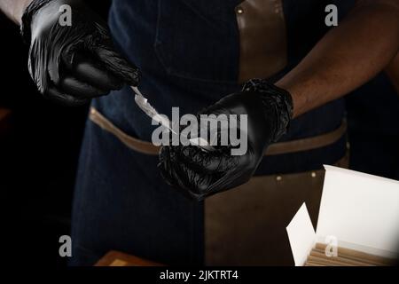 Un primo piano delle mani di un uomo che indossa guanti di plastica neri, tenendo un tovagliolo di carta Foto Stock