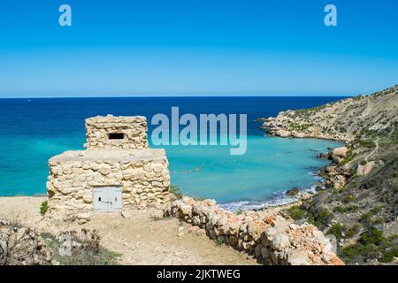 Vecchio posto militare sulla spiaggia che protegge Imgiebah Bay, vicino Selmun, Mellieha, Malta. Le onde blu del mare Mediterraneo sulla spiaggia di sabbia in questo luogo remoto. Foto Stock